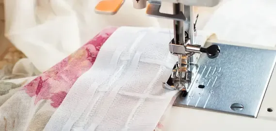 Close-up of a sewing machine stitching white fabric with a floral pattern