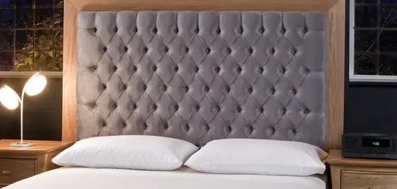 Elegant grey tufted headboard mounted on wooden frame with white bedding
